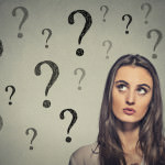 Portrait thinking young business woman looking up at many question marks isolated on gray wall background