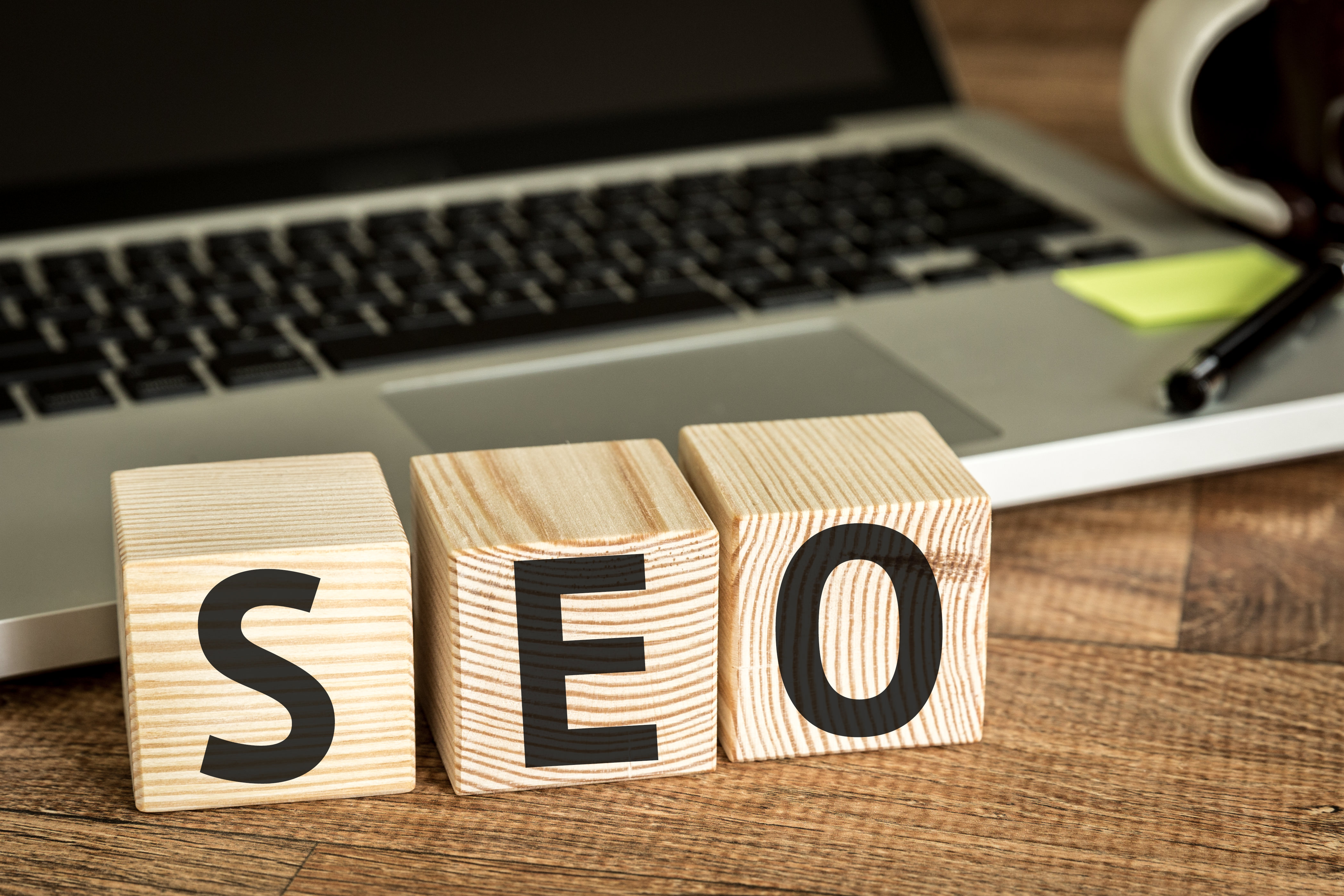 SEO (Search Engine Optimization) written on a wooden cube in front of a laptop